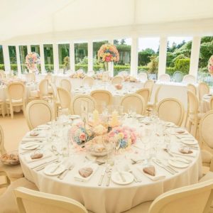 Internal photo showing banqueting tables, dressed with white linens, cutlery, crockery and centrepiece flowers. View of gardens visible through windows.