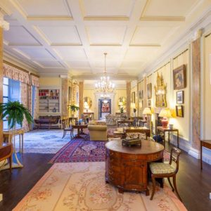 State Drawing Room with wooden floor and a variety of persian rugs and furniture from the Royal Collection. A variety of Irish art hangs on the sunny yellow walls. Marble-like pillars frame the room.